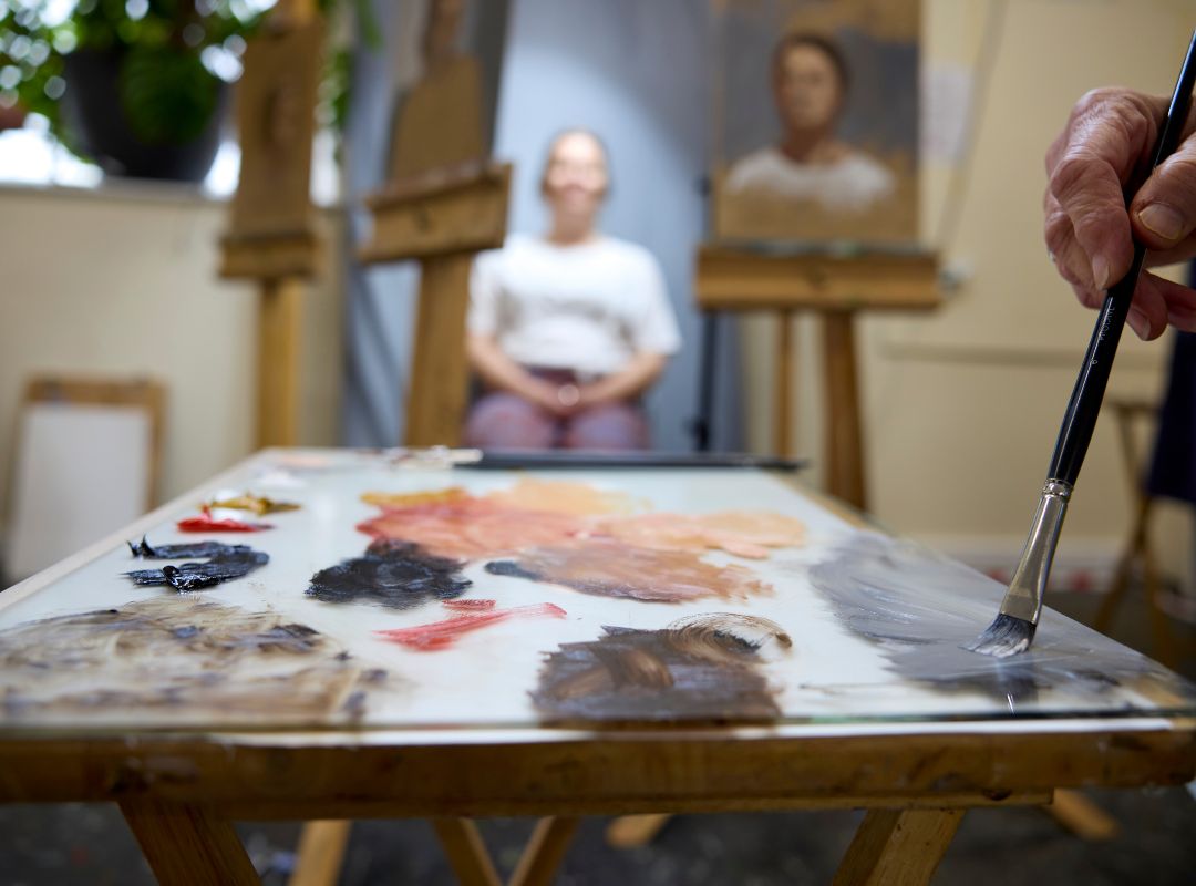 An artist palette covered in oil paint in front of a portrait model sitting for an artist An artist palette covered in oil paint in front of a portrait model sitting for an artist